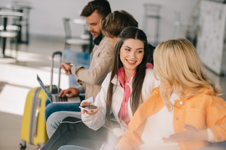 Young friends talking while waiting for flight in airport terminalの写真素材