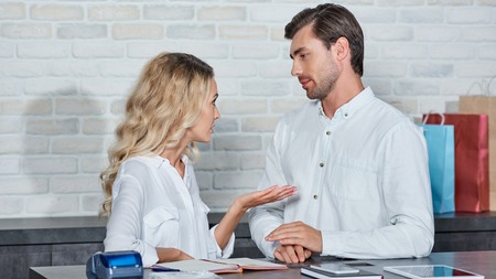 Young coworkers talking and looking at each other while working together in storeの写真素材