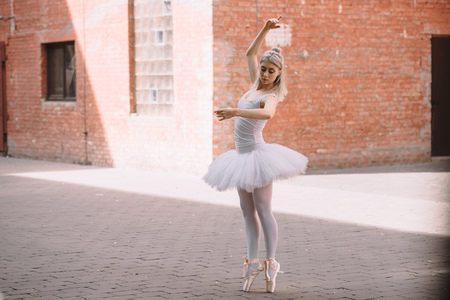 Young ballerina in white tutu and pointe shoes dancing on streetの写真素材