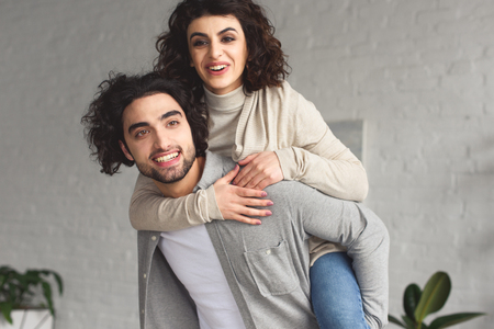 Boyfriend giving piggyback to smiling girlfriend at homeの写真素材