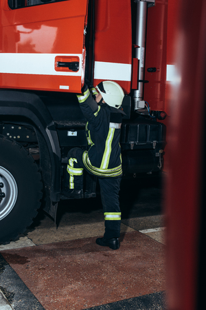 Female firefighter in protective uniform getting into truck at fire stationの写真素材
