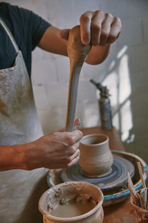 Cropped image of professional potter in apron working with clay at pottery studioの写真素材