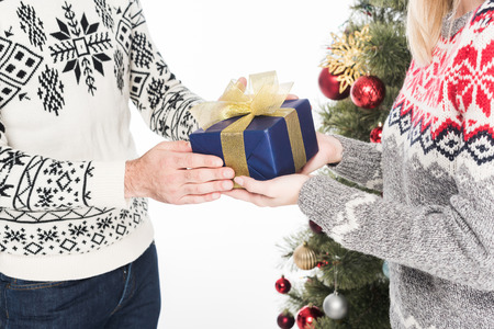 Cropped shot of man presenting wrapped gift to girlfriend at Christmas tree isolated on white backgroundの写真素材