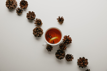 Flat lay with pine cones and cup of hot tea on white backdropの写真素材