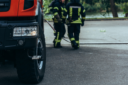 Partial view of brigade of firefighters and water hose on ground on streetの写真素材
