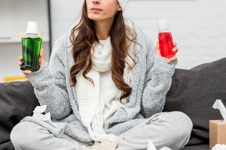 Cropped shot of sick young woman in warm clothes choosing between red and green bottles of gargling liquids at homeの写真素材