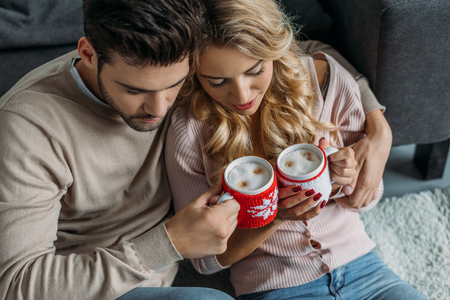 High angle view of couple clinking with cups of cappuccino at home, Christmas conceptの写真素材