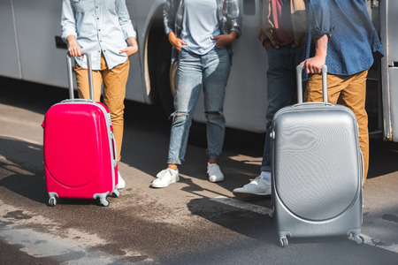 Cropped image of tourists with wheeled bags standing near travel bus at streetの写真素材