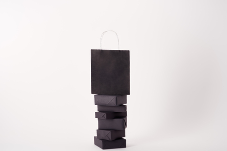 Black shopping bag on stacked boxes on white surface, black Friday conceptの写真素材