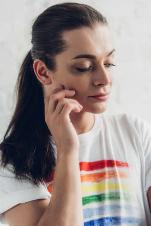 Close-up portrait of young transgender man in white t-shirt with pride flag in front of white brick wall backgroundの写真素材