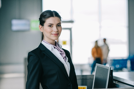 Attractive young woman smiling at camera while working at check-in desk in airportの写真素材