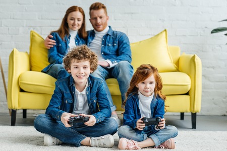 Children playing video game while parents sitting on sofaの写真素材