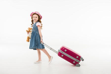 Little stylish child with teddy bear and suitcase isolated on white background, travel conceptの写真素材