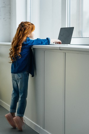 Adorable child reaching to laptop on windowsillの写真素材