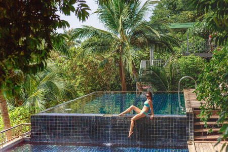 Beautiful girl in bikini relaxing on poolside at tropical resort