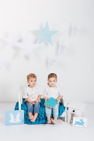 Adorable little kids sitting on blue knitted plaid with book and rabbit cards, Easter conceptの写真素材