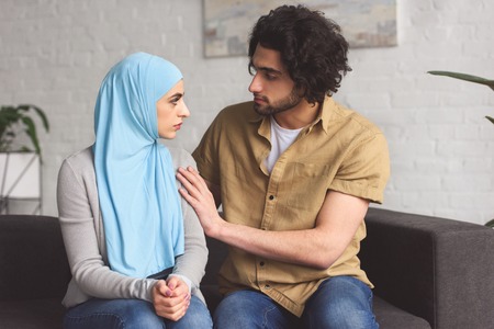 Muslim boyfriend hugging girlfriend in hijab in living roomの写真素材