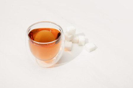 Close-up view of glass cup with fresh herbal tea and sugar cubes on grey background