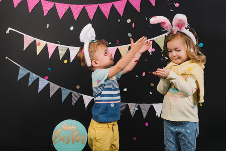 Adorable little kids with bunny ears throwing confetti on black background, Easter conceptの写真素材