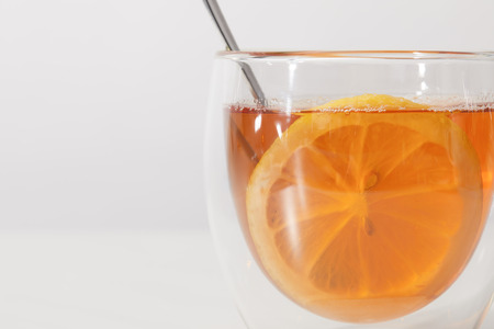 Close-up view of glass cup with fresh hot tea, spoon and slice of lemon on grey backgroundの写真素材