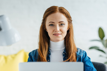 Smiling young woman looking at camera by laptopの写真素材