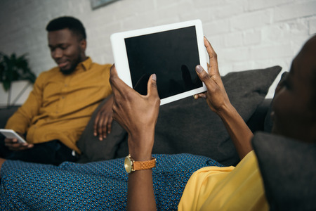 Cropped shot of young woman lying on sofa with digital tablet while boyfriend using smartphoneの写真素材