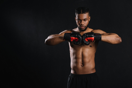 Muscular shirtless African American boxer in boxing gloves looking at camera isolated on black backgroundの写真素材