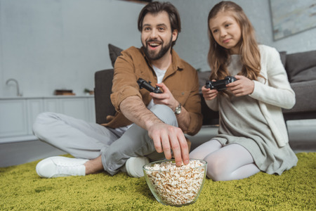 Father playing video game with daughter and eating popcornの写真素材