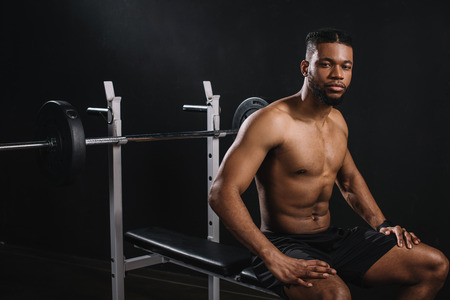 Handsome muscular shirtless young sportsman sitting and looking at camera