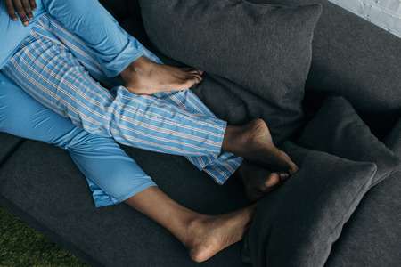 Low section of young couple in pajamas lying together on sofa