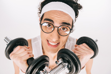 Young skinny sportsman in eyeglasses holding dumbbells isolated on white backgroundの写真素材