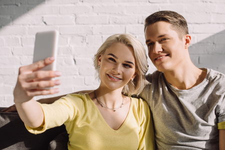 Smiling couple taking selfie with smartphone at homeの写真素材