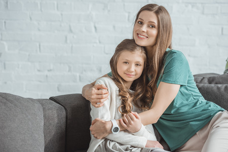 Happy mother and daughter hugging and looking at camera at home