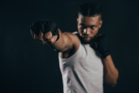 Close-up view of young African American kickboxer training on black backgroundの写真素材