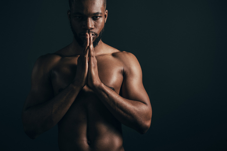 Serious shirtless young African American sportsman looking at camera isolated on black backgroundの写真素材