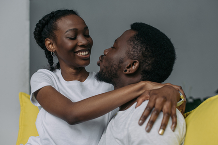 Beautiful young African American couple hugging and smiling each other at homeの写真素材