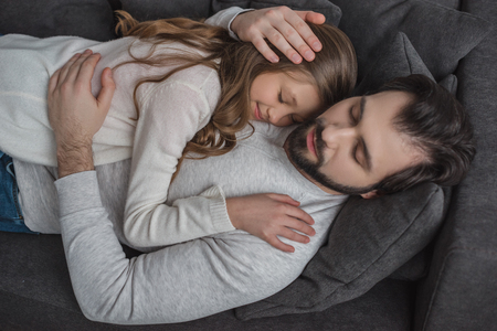 High angle view of father and daughter sleeping on sofaの写真素材