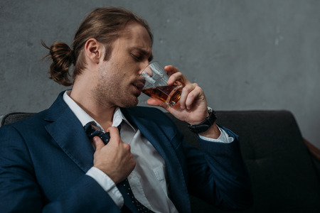 Young alcohol addicted businessman drinking whiskeyの写真素材