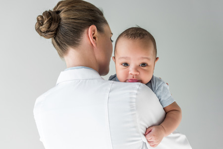 Rear view of female pediatrician with African American baby isolated on grey backgroundの写真素材
