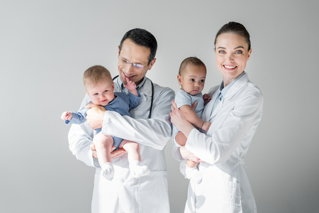 Happy adult pediatricians holding little babies isolated on grey backgroundの写真素材