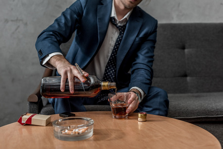 Cropped shot of alcohol addicted businessman drinking whiskey while sitting on couchの写真素材