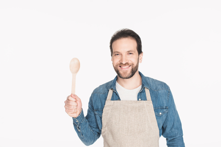 Portrait of smiling man in apron with wooden spoon isolated on white backgroundの写真素材