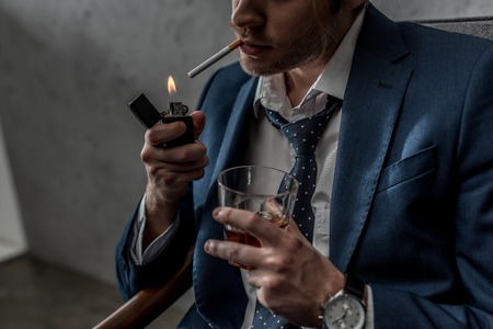 Cropped shot of businessman with glass of whiskey smoking cigaretteの写真素材
