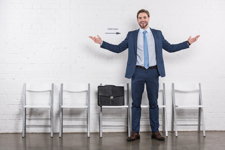 Happy Caucasian businessman standing near empty chairs while waiting for job interviewの写真素材