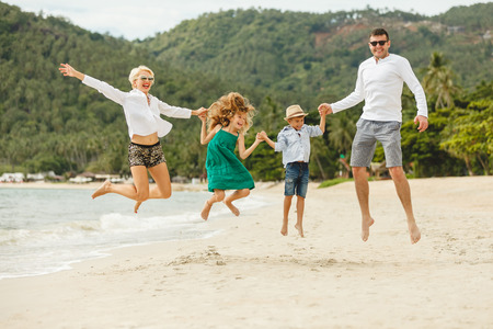 Beautiful happy family on vacation jumping together on tropical beachの写真素材