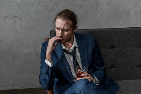 Drunk alcohol addicted businessman with glass of whiskey smoking cigaretteの写真素材