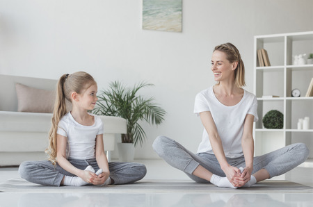 mother and daughter practicing yoga in butterfly pose at homeの写真素材