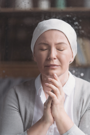 portrait of sick mature woman in kerchief praying with closed eyes