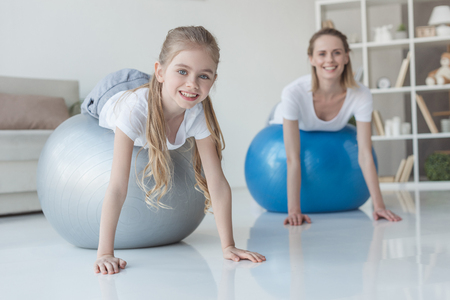 Smiling mother and daughter lying on fit balls at homeの写真素材