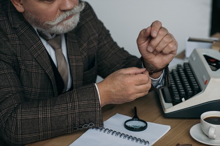 Cropped shot of senior writer putting on his vintage watch at workplace